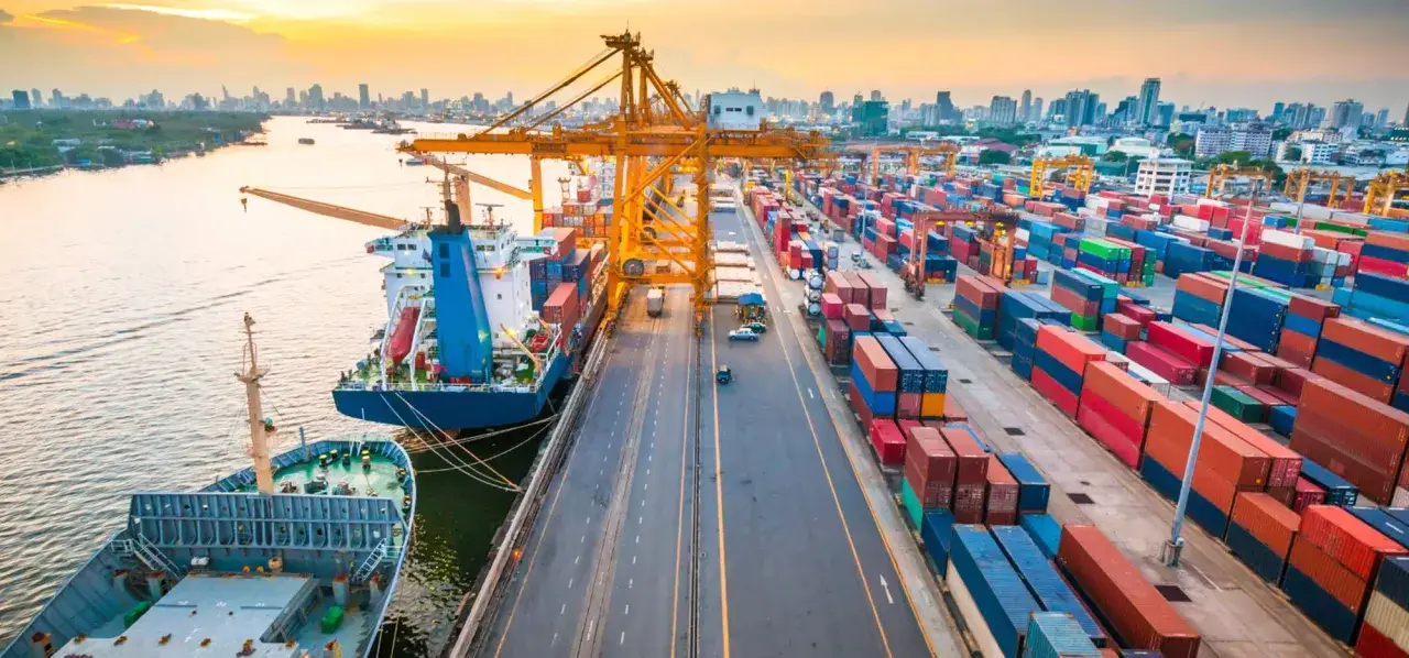 Ein gesch&auml;ftiger Hafen bei Sonnenuntergang, mit Schiffen, Kr&auml;nen und Containern, die das maritime Management veranschaulichen.