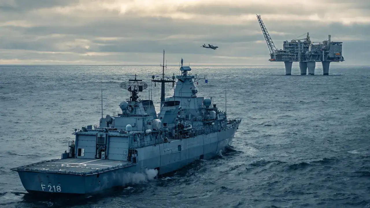 Ein Kriegsschiff F 218 patrouilliert vor einer Ölplattform, während ein Flugzeug am Himmel fliegt. Dies unterstreicht die maritime Sicherheit.