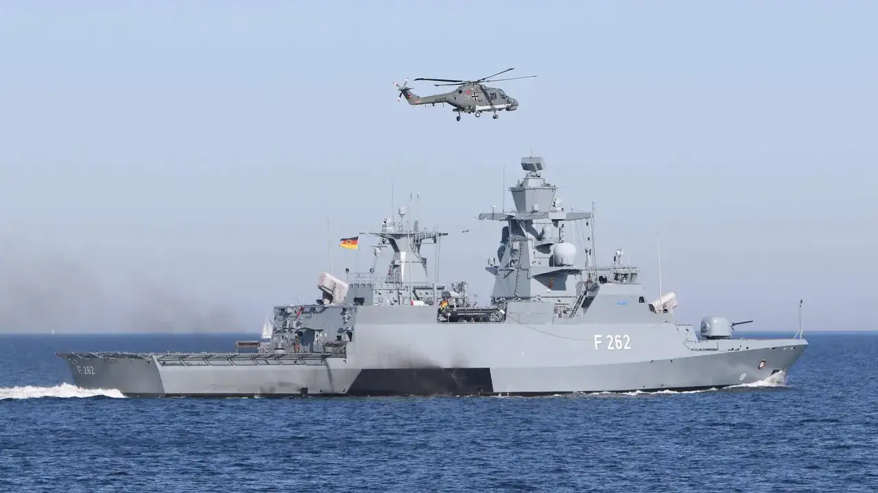 Ein deutsches Marinehubschrauber fliegt &uuml;ber der Fregatte F 262, einer modernen corvette ship, auf dem Meer.