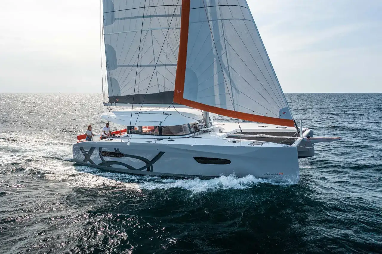 Zwei Personen steuern eine graue Katamaran-Segelyacht, die