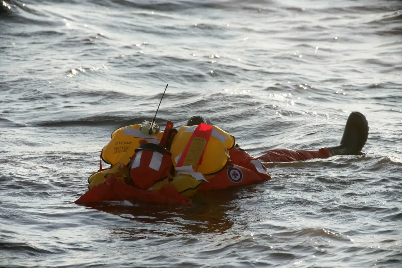 Mann über Bord! Eine Person in Rettungsweste treibt im Wasser, ein Bein ragt heraus.