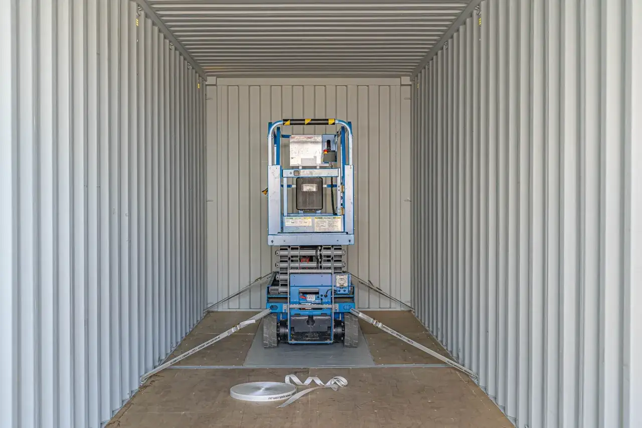 Blauer Hubsteiger im Container, gesichert mit Spanngurten f&uuml;r sicheren Transport. Container lashing ist hier essenziell.