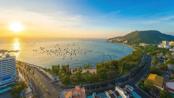 Sonnenuntergang über dem Vung Tau Port mit vielen Booten im Wasser und einer grünen Hügelkette im Hintergrund.