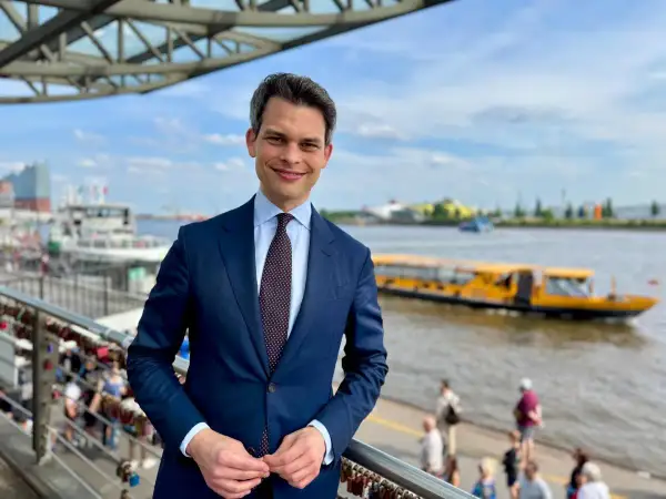 Ein Mann im Anzug steht am Hafen. Im Hintergrund fährt ein gelbes Ausflugsboot. Er ist ein port agent, der die Schiffe im Blick hat.