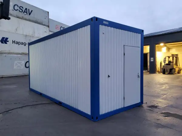 Ein blauer und weißer Container steht auf einem Container-Depot. Im Hintergrund sind weitere Container und ein Gabelstapler zu sehen.