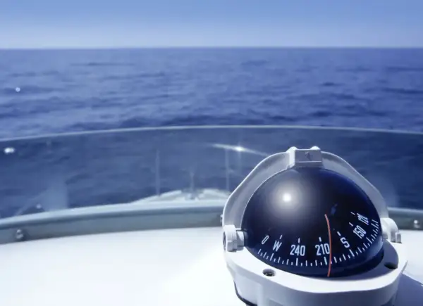 Kompass auf einem Boot zeigt die Richtung auf dem Meer. Teile des Bootes wie das Deck und die Windschutzscheibe sind sichtbar.