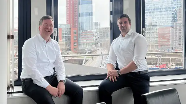 Zwei Männer, ein maritimer Anwalt und sein Kollege, sitzen vor einem Fenster mit Blick auf die Hamburger Hafencity.
