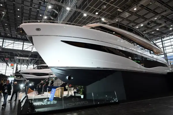 Eine glänzende weiße Luxus-**Boot**-Yacht mit dunklen Fenstern, ausgestellt auf einer Messe. Im Hintergrund eine weitere Yacht und Besucher.