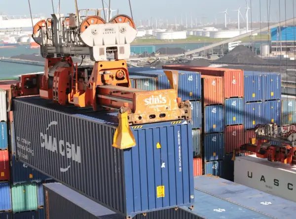 Ein Kran hebt einen blauen CMA CGM-Container. Viele weitere Container stapeln sich im Hafen, kein Container ist unberührt.