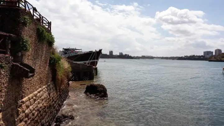 Ein Schiff liegt im Hafen von Mombasa vor Anker. Die Steinküste und Gebäude im Hintergrund zeugen von der geschäftigen Atmosphäre.